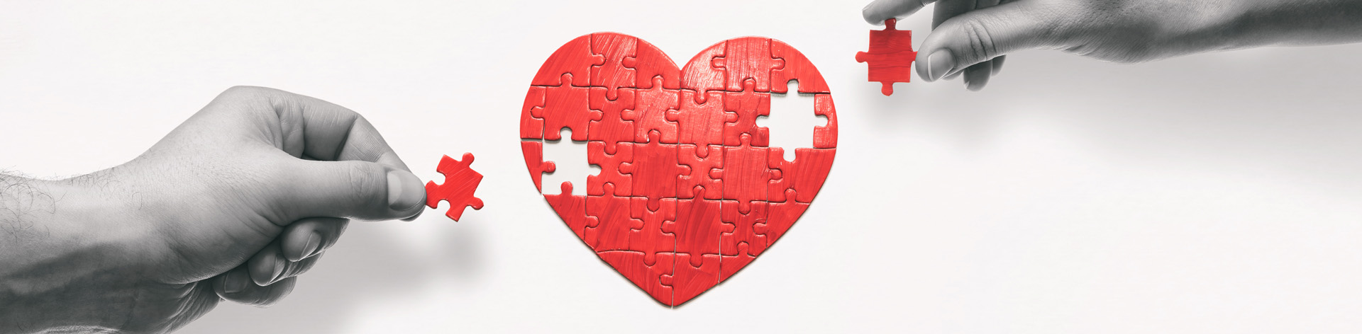 Two hands work together to finish a red heart puzzle.